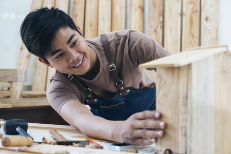 DIY woodworking and furniture making and craftsmanship and handwork concept. Carpenter working on woodworking machines in carpentry shop. Young man working as carpenter and taking wood stock.の写真素材