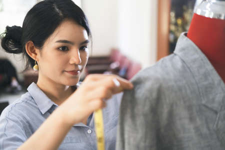 Closeup young woman tailor taking measurements of jacket on mannequin.の写真素材