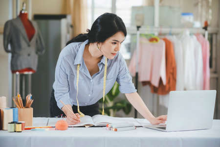 Young female fashion designer using computer and drawing sketches for new collection.
