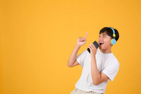 Happy young man singing while using earphones and mobile phone isolated over yellow background.の写真素材