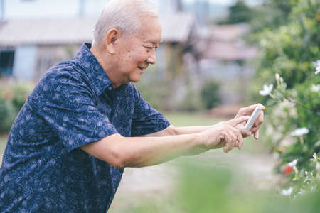 Happy asian senior man in the graden taking a picture with mobile phone. Happy retirement life.の写真素材