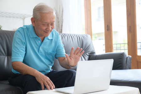 Elderly man making video call and waving at screen, chatting with children, communication with...