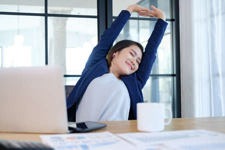 Woman twisting the body to relax while sitting as she sits at her desk after working all day.の写真素材