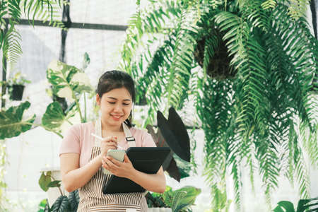 Young woman plant shop owner is checking customer order from websiteの写真素材