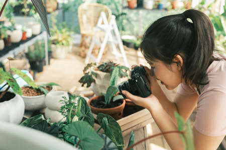 Smiling young woman taking smartphone picture of plant in a small shop