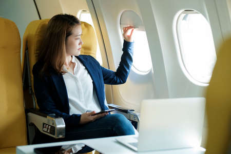 Business woman In a plane, works on using laptop computer and phone, look in the plane window.の写真素材