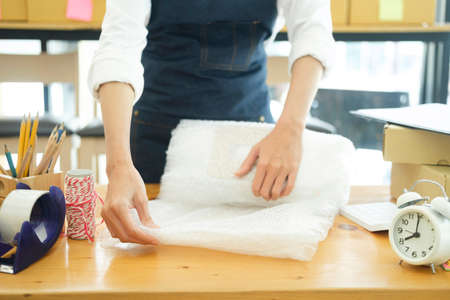 Asian female clothes shop owner folding a t-shirt and packing in a cardboard parcel box.
