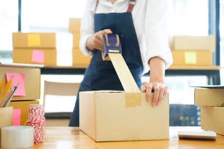 Asian female clothes shop owner folding a t-shirt and packing in a cardboard parcel box.