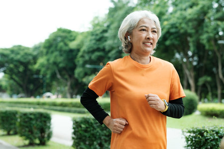 Athletic asian senior woman running outdoor jogging in park.の写真素材