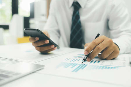 Young Asian startup businessman using smartphone to analyze online marketing information.