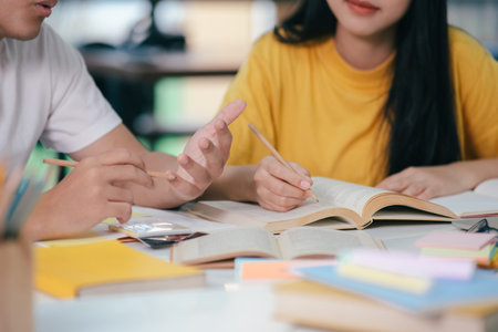 Young asian university students are studying for an exam. There are tutor books with friends. They are classmates that try to help each other. They have been tutoring for many hours in the campus.の写真素材