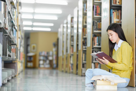 Young female college highschool student in casual clothings sitting on the floor reading book, studying and doing research for school project at a library. Learning, Education, Library concept.の写真素材