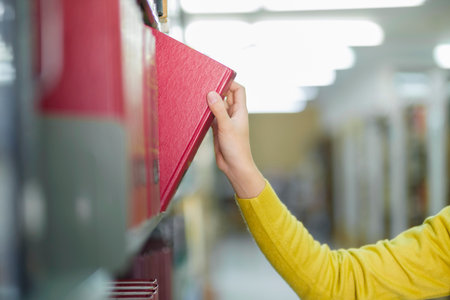 Young asian female student in casual outfit standing, looking and choosing books to read at library for studying, academic research, or school work or project. Learning, Education, Library concept.の写真素材