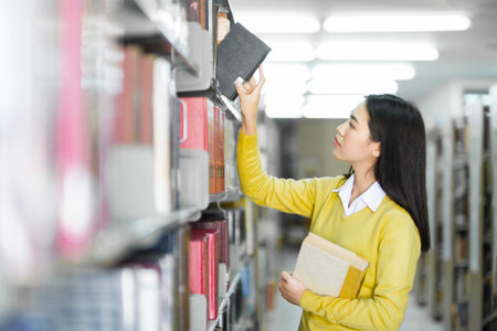 Young asian female student in casual outfit standing, looking and choosing books to read at library...