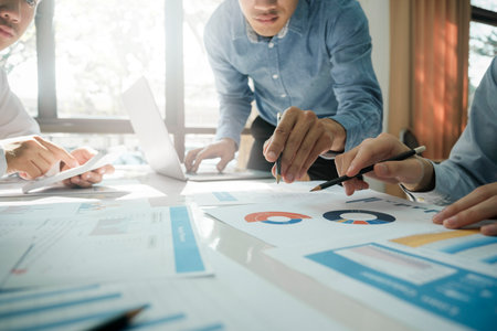 Close-up of businessmen working together at workplace, discussing about strategies, plans, analytic progress, and financial stats, and pointing at graph documents on desk holding pencils and calculator. Business and Teamwork concept.の写真素材