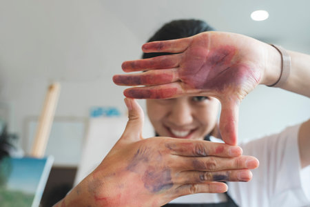 The artist creates a frame with her hands soiled with watercolor paints.