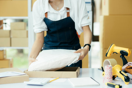 Small business owner packing clothes in the box at workplace.