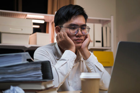 Asian young tired staff businessman using desktop computer having overwork project overnight in...