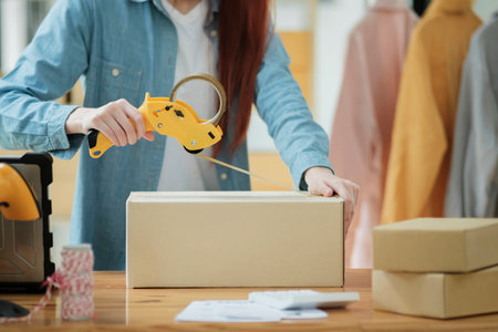 Woman packing box, package and cargo with tape for delivery, sale and shipping in workshop, startup store and creative studio.の写真素材