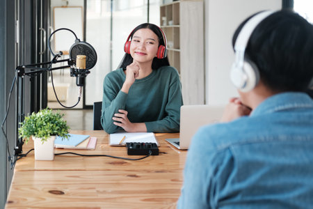 A woman is sitting at a desk with a microphone and a laptopの写真素材