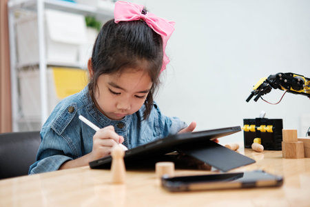 Concentrated young girl in denim using a stylus pen to draw on a digital tablet, embracing technology in education.の写真素材