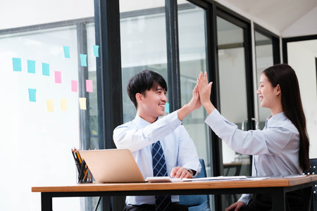 Two elated business colleagues giving a high-five over a successful project at their office workspace.の写真素材