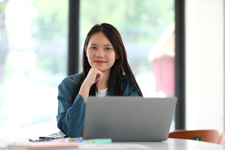 A woman is sitting at a table with a laptop in front of herの写真素材