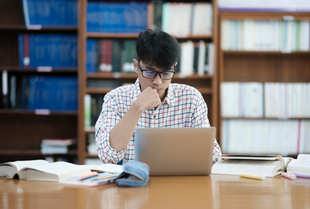 Young Asian male sitting inside a library alone doing research. Man working on a project. Young man doing research for a case.の写真素材