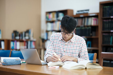 Young Asian male sitting inside a library alone doing research. Man working on a project. Young man doing research for a case.の写真素材