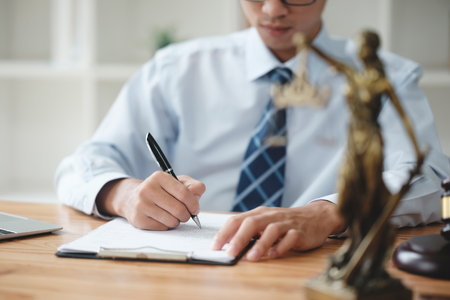 A lawyer in a suit is sitting at his desk, signing legal documents with a gavel on the side.の写真素材