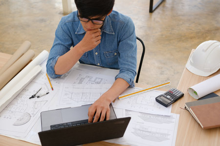 Architect and engineer working on a laptop with blueprints at a desk in an officeの写真素材