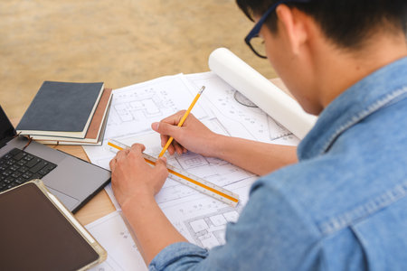 Architect and engineer drafting blueprints with a pencil and ruler at a work desk