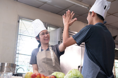 Two smiling chefs giving a high five in a kitchen after a successful cooking session