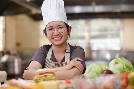 Culinary student standing confidently in training kitchen with fresh ingredients ready for cooking practiceの写真素材