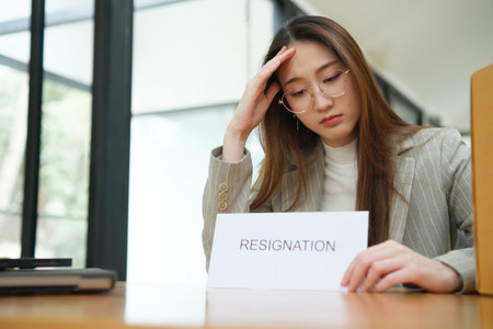 Unemployed woman with resignation letter and office box showing stress after layoffの写真素材