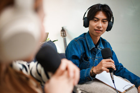 Young man speaking in podcast with headphones and microphone at homeの写真素材