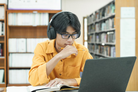 Young college student using computer and mobile device studying online.