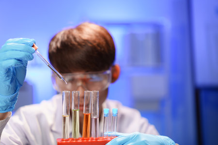 Scientists working in Laboratory using pipette dropping liquid sample into test tube.