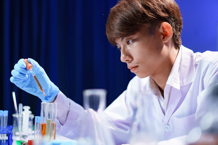 Scientists working in Laboratory using pipette dropping liquid sample into test tube.