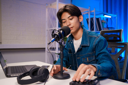 Podcast creator adjusting audio mixer in home studio with microphone and laptopの写真素材