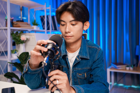 Young man adjusting microphone for podcast recording in home studioの写真素材