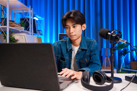Podcast host preparing live recording in professional studio with microphone and laptopの写真素材