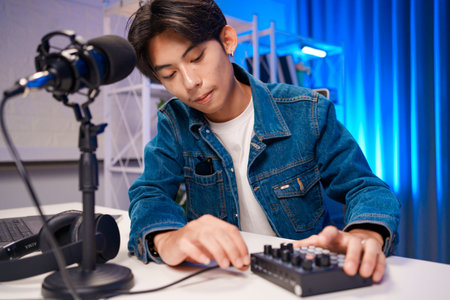 Podcast creator adjusting audio mixer in home studio with microphone and laptopの写真素材
