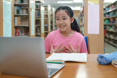 School student girl having video call on her computer in library at school.