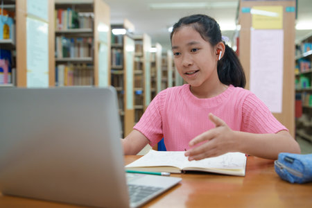 School student girl having video call on her computer in library at school.