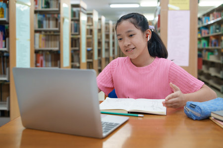 School student girl having video call on her computer in library at school.