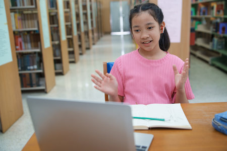 School student girl having video call on her computer in library at school.