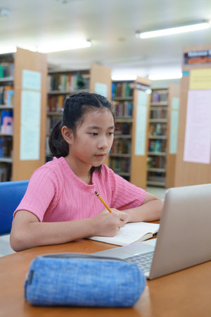 Student learning online class by using laptop computer and writing notebook at workplace, E learning...