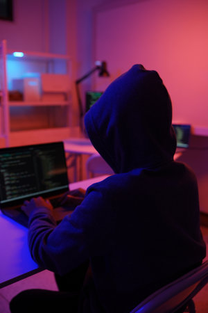 A mysterious hooded hacker working on a computer in a dark room.の写真素材