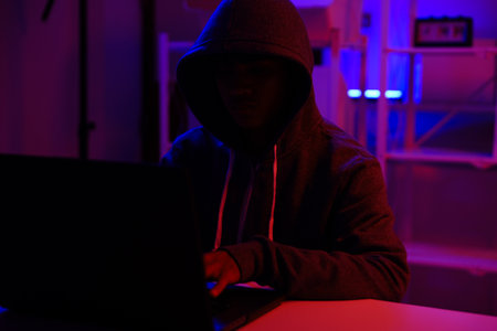 A mysterious hooded hacker working on a computer in a dark room.